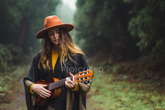 Jovem mulher de chapéu jogando ukulele na natureza — Fotografia de Stock