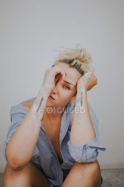 Femme blonde en chemise masculine touchant le visage avec les bras en peinture — Photo de stock