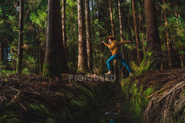 Vista lateral da jovem mulher pulando sobre o dreno na floresta — Fotografia de Stock