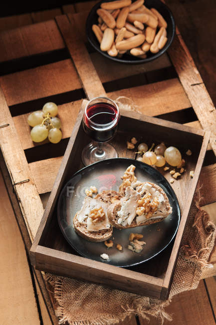 Brotscheiben mit Käse im Teller und Wein auf Holztablett — Stockfoto