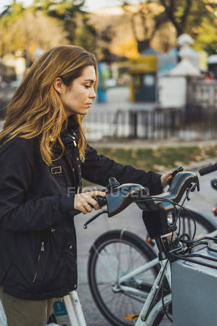Young pretty woman taking bicycle from parking in park. — Stock Photo