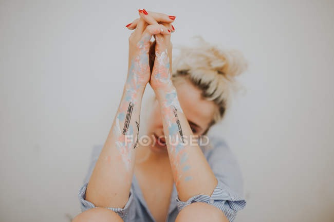 Pretty blonde woman with painted and tattooed arms at gray wall. — Stock Photo