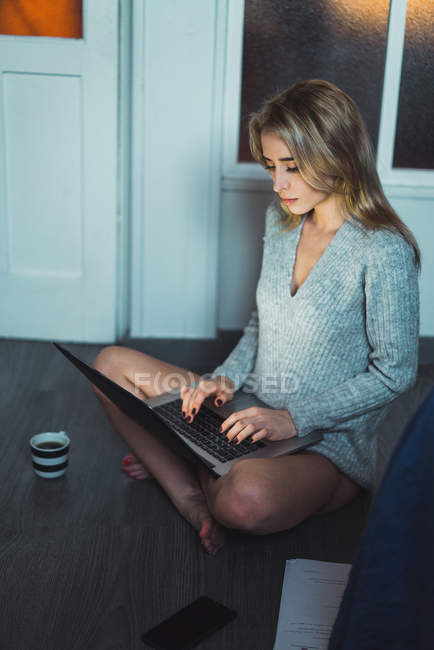 Блондинка сидить на підлозі вдома і використовує ноутбук — стокове фото
