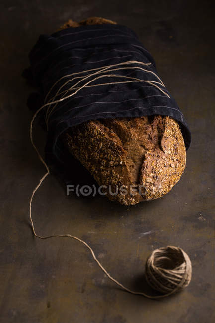 Freshly baked bread wrapped in towel and tighten with spool of thread on dark background — Stock Photo