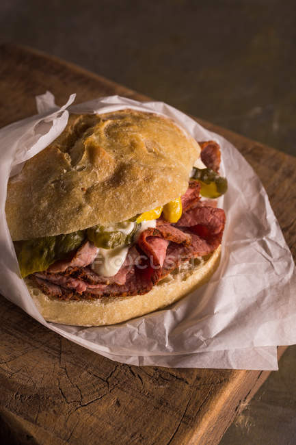 Delicious pastrami sandwich with pickles and mustard wrapped in paper — Stock Photo