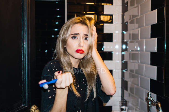 Traurige Blondine posiert mit Zahnbürste im Badezimmer — Stockfoto