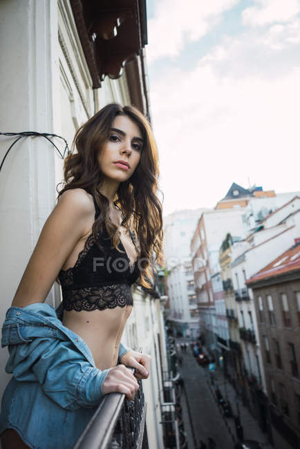 Young woman in black lingerie looking at camera and leaning on balcony handrail — Stock Photo