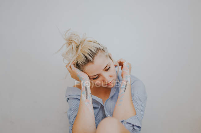 Attraente donna bionda in camicia con le braccia dipinte seduta al muro grigio
. — Foto stock