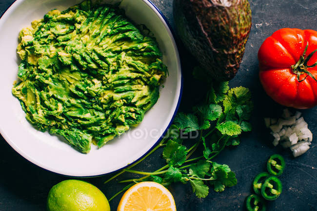 Bol de guacamole avec des ingrédients sur le bureau — Photo de stock