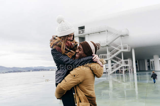 Felice giovane uomo che abbraccia e tiene a mezz'aria fidanzata al porto . — Foto stock