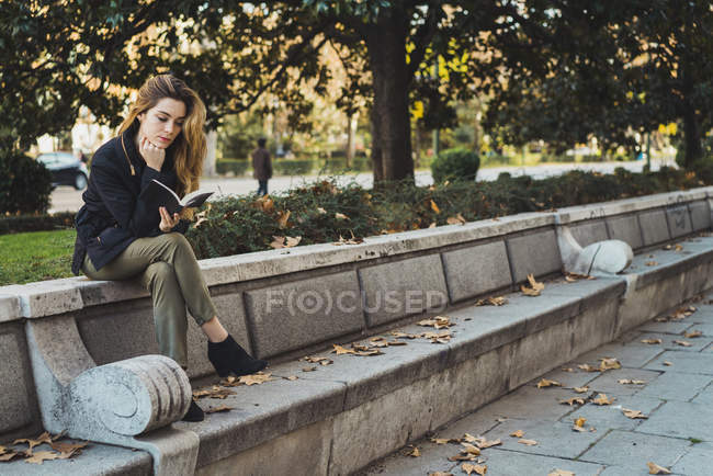 Frau sitzt auf Steinbank und liest Buch im Park — Stockfoto