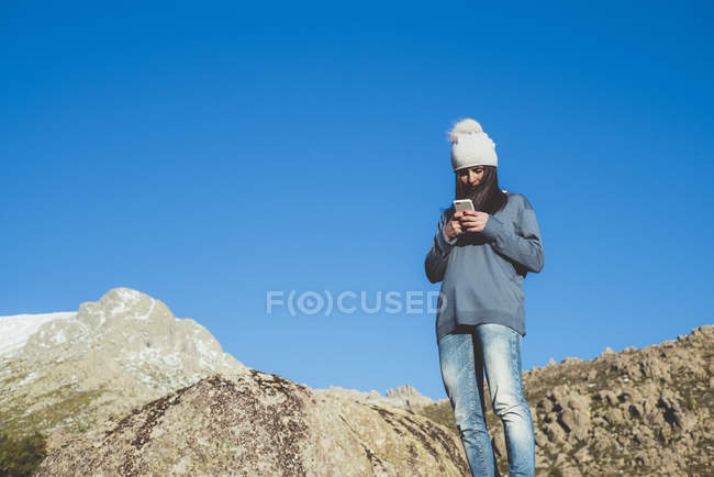 Donna che naviga smartphone su roccia contro cielo — Foto stock