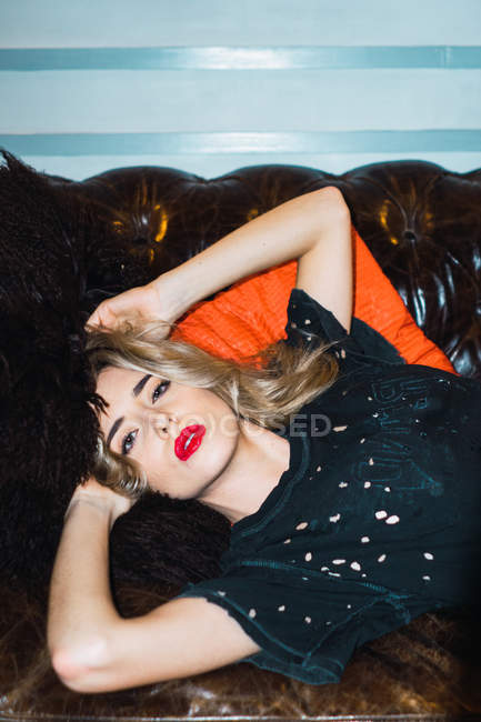 Blondine liegt auf Couch und blickt in Kamera — Stockfoto