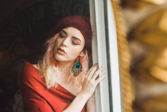 Jeune jolie femme aux cheveux roses debout à la fenêtre et regardant loin . — Photo de stock
