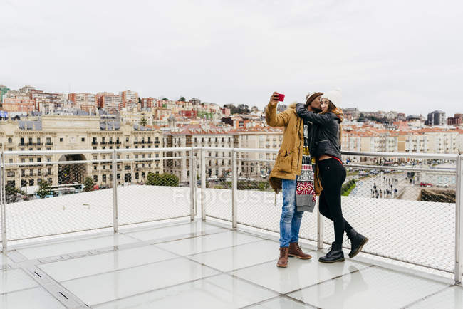 Casal sorridente tomando selfie contra a paisagem urbana — Fotografia de Stock