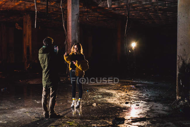 Visão traseira do fotógrafo atirando mulher com tocha de iluminação no prédio abandonado — Fotografia de Stock