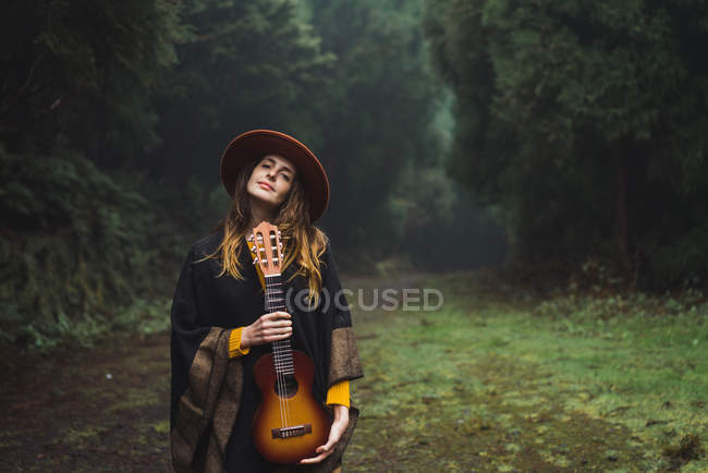 Charming woman posing with ukulele at misty woods — Stock Photo
