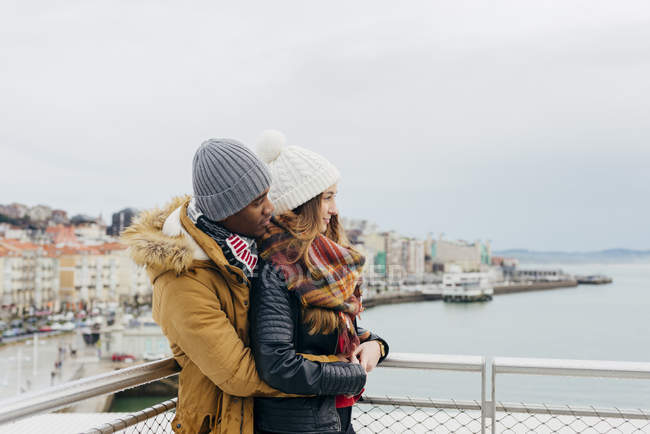 Cheerful couple embracing and looking at ocean at harbor — Stock Photo