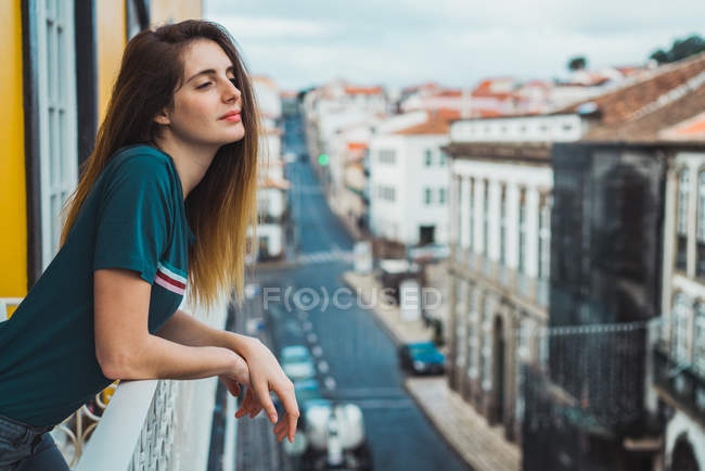 Seitenansicht einer Frau, die sich an einen Balkonzaun lehnt und die Stadt erkundet. — Stockfoto