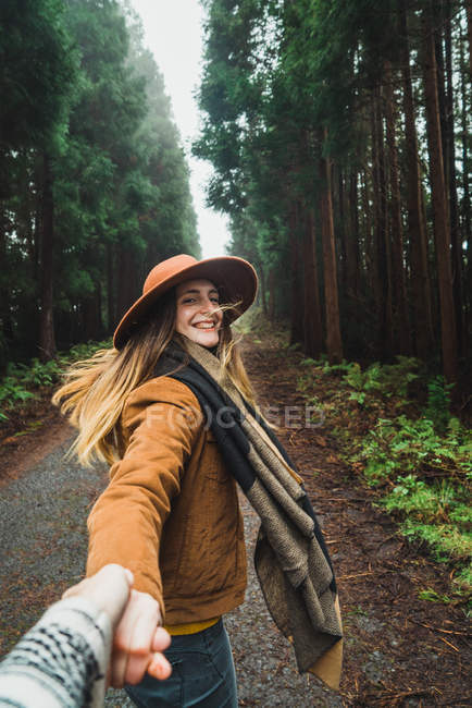 Mujer cogida de la mano del fotógrafo y sígueme haciendo gestos en el bosque - foto de stock