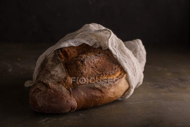 Freshly baked bread covered with towel on dark background — Stock Photo