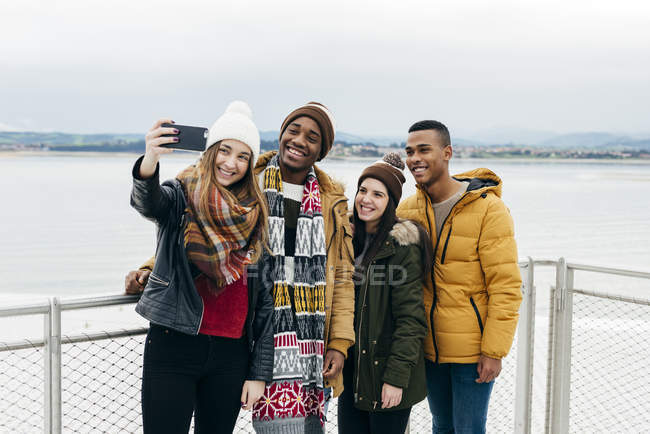 Allegro multirazziale amici in piedi in porto e prendendo selfie insieme . — Foto stock