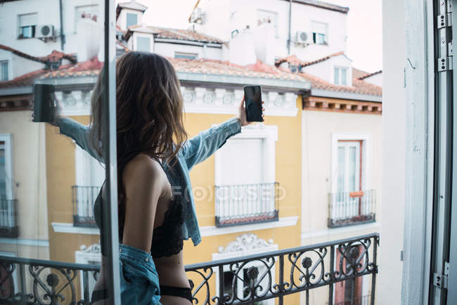 Женщина в нижнем белье делает селфи на балконе — стоковое фото