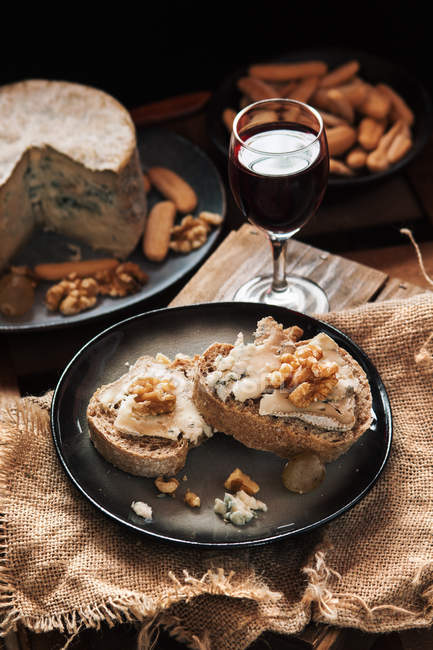 Fatias de pão com queijo e nozes em prato por copo de vinho — Fotografia de Stock