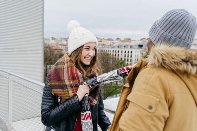 Fröhliche Frau zieht Schal ihres Freundes vor dem Hintergrund der Stadt. — Stockfoto
