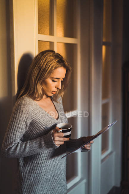 Shocked woman with cup reading papers — Stock Photo