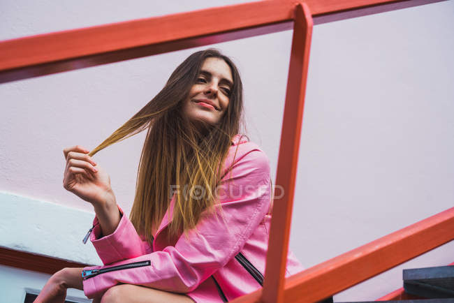 Молода жінка сидить на сходах і грає з волоссям — стокове фото
