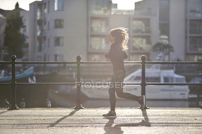 Vista lateral de la mujer corriendo en la calle puesta del sol - foto de stock