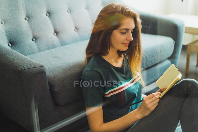 Молода жінка сидить на підлозі з блокнотом вдома — стокове фото