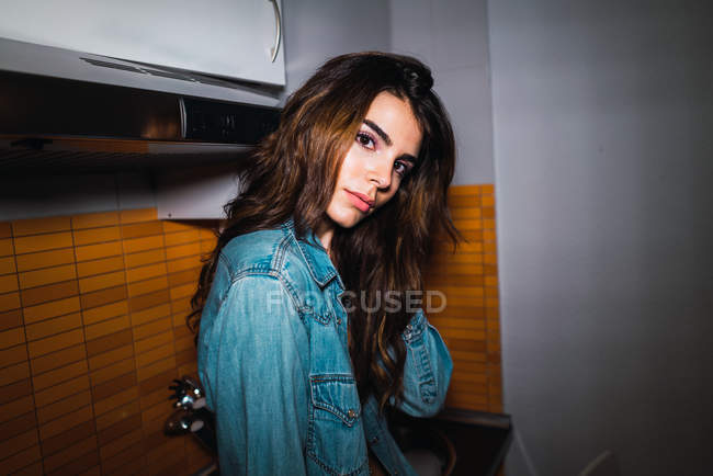 Woman in jeans jacket posing by kitchen table — Stock Photo