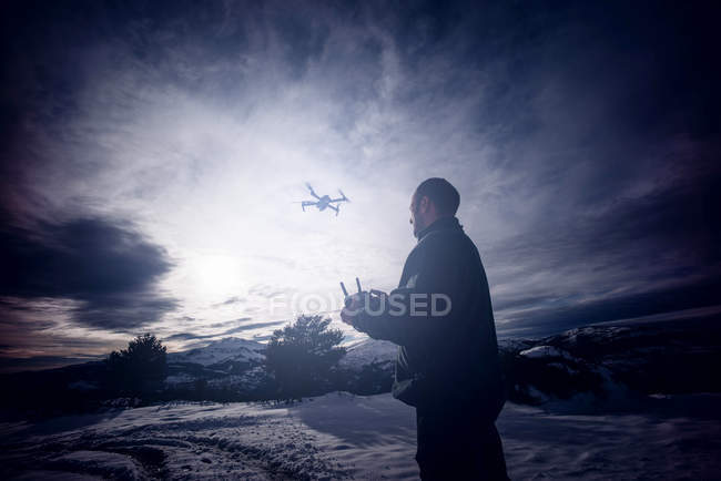 Mann fliegt Drohne mit Fernbedienung in verschneiter Landschaft. — Stockfoto