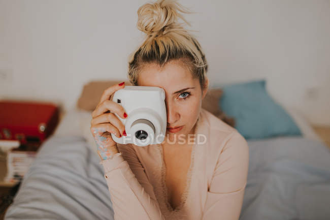 Junge Frau mit Sofortkamera sitzt auf dem Bett. — Stockfoto