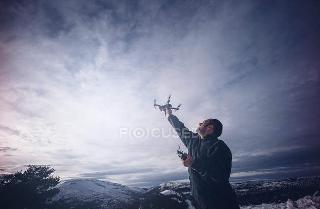 Man trying to catch flying drone in snowy landscape. — Stock Photo