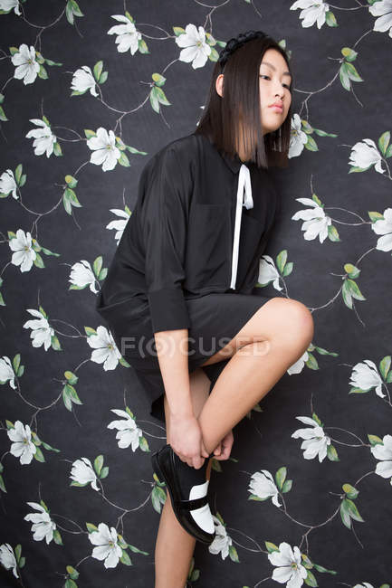 Pretty woman in black dress wearing shoe on floral backdrop — Stock Photo
