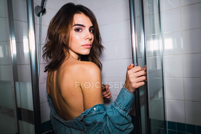 Mujer joven quitándose la camisa vaquera para tomar la ducha en el baño . - foto de stock