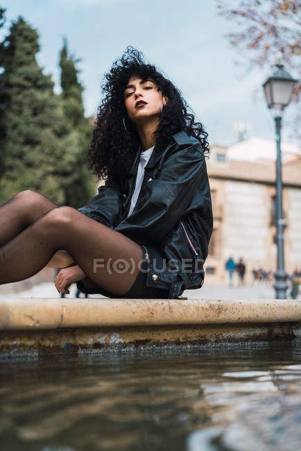 Junge Frau sitzt am Brunnen und blickt in die Kamera — Stockfoto