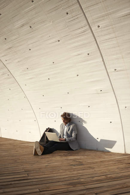 Businessman sitting at wooden passage and using laptop — Stock Photo
