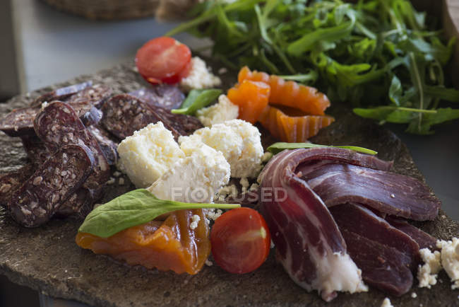 Tasty meat snacks with cheese and vegetables served on stone plate. — Stock Photo