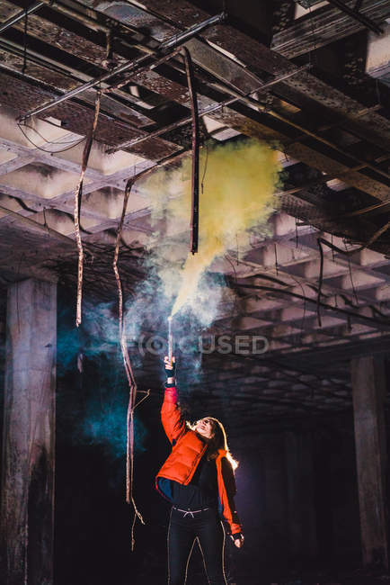 Woman with blue smoking torch in outstretched hand posing at abandoned building — Stock Photo