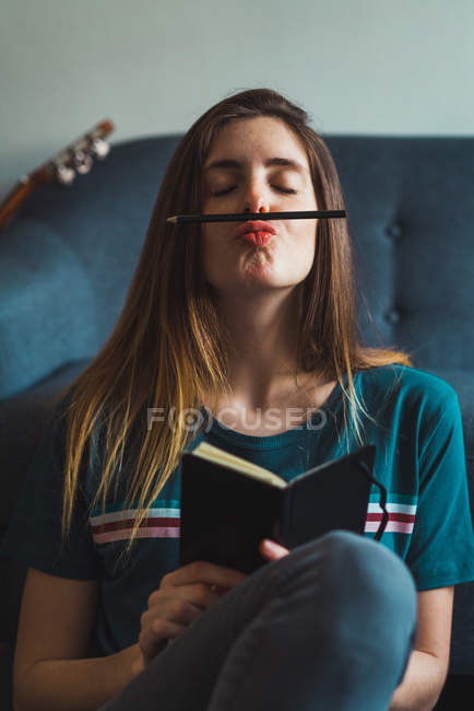 Молода брюнетка сидить з блокнотом на підлозі, тримаючи олівець між губами і носом . — стокове фото