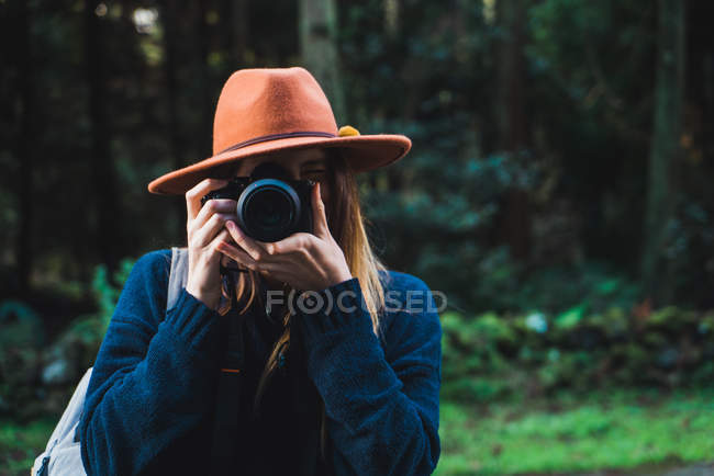 Mujer con sombrero tomando fotos en el bosque - foto de stock