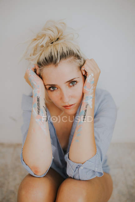 Attractive woman in male shirt sitting by wall and looking at camera — Stock Photo