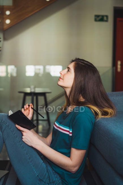 Молода жінка сидить на підлозі з блокнотом і дивиться вгору — стокове фото