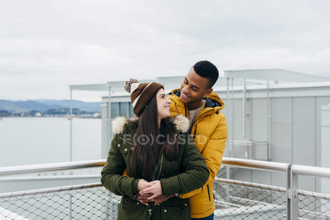 Smiling young couple embracing at fence on background of ocean. — Stock Photo