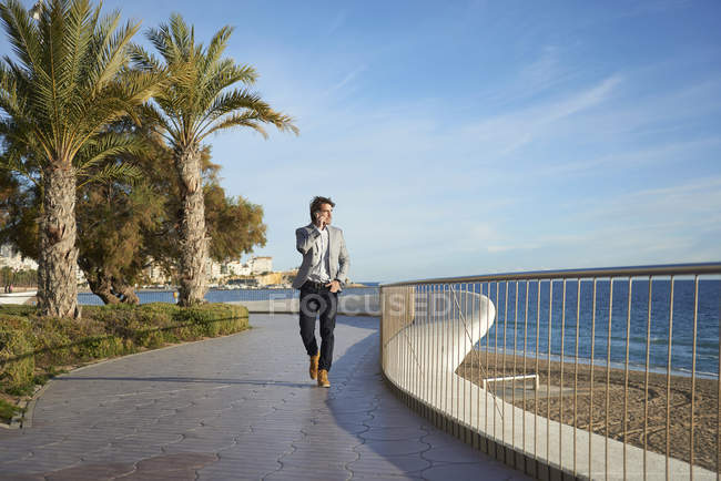 Businessman walking along sea and talking on smartphone — Stock Photo