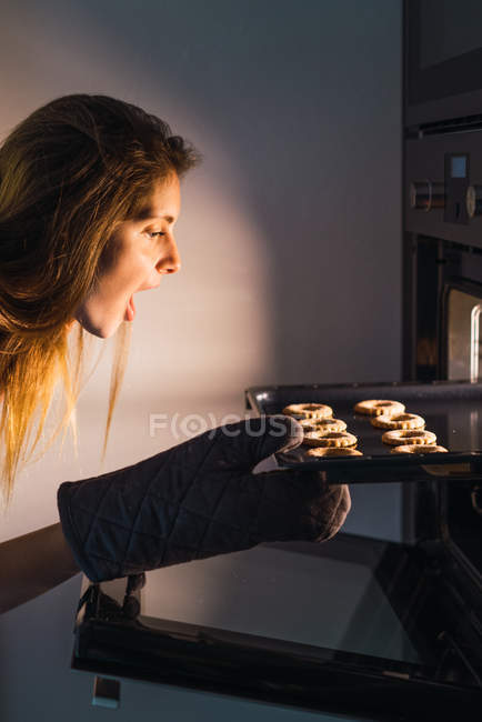 Exited woman taking cookies out of oven — Stock Photo